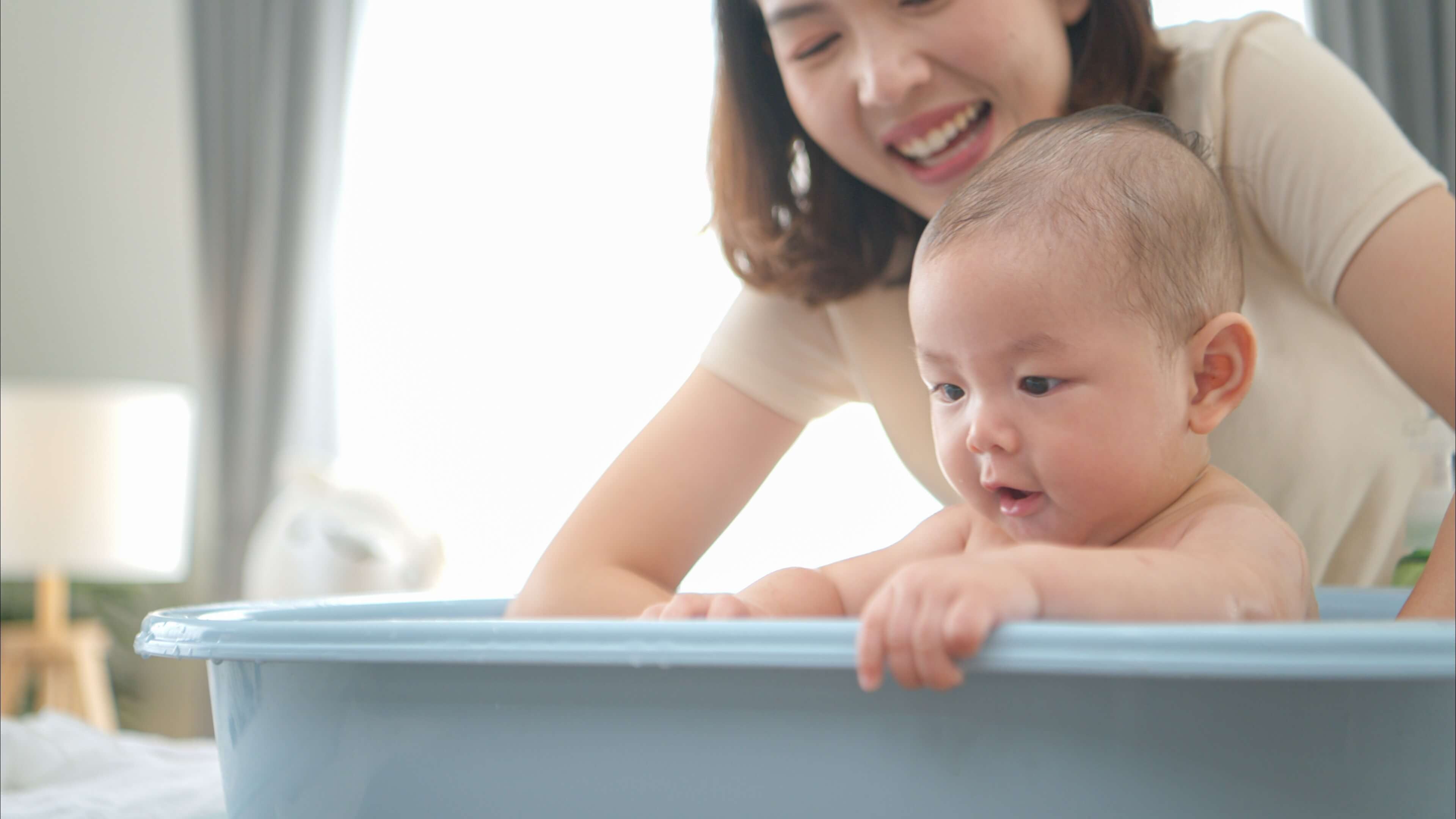 mom washing baby sitting in baby bathtub