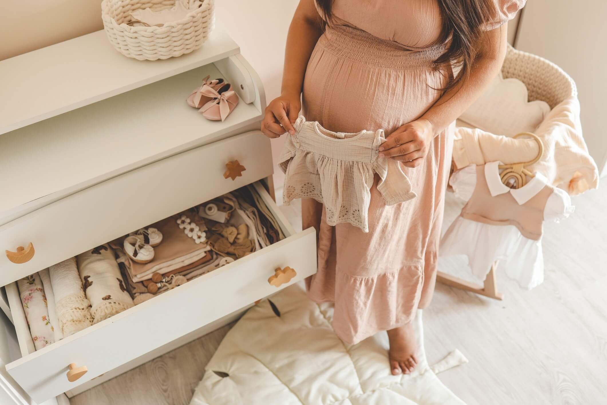 pregnant mom holding baby clothes from dresser in nursery